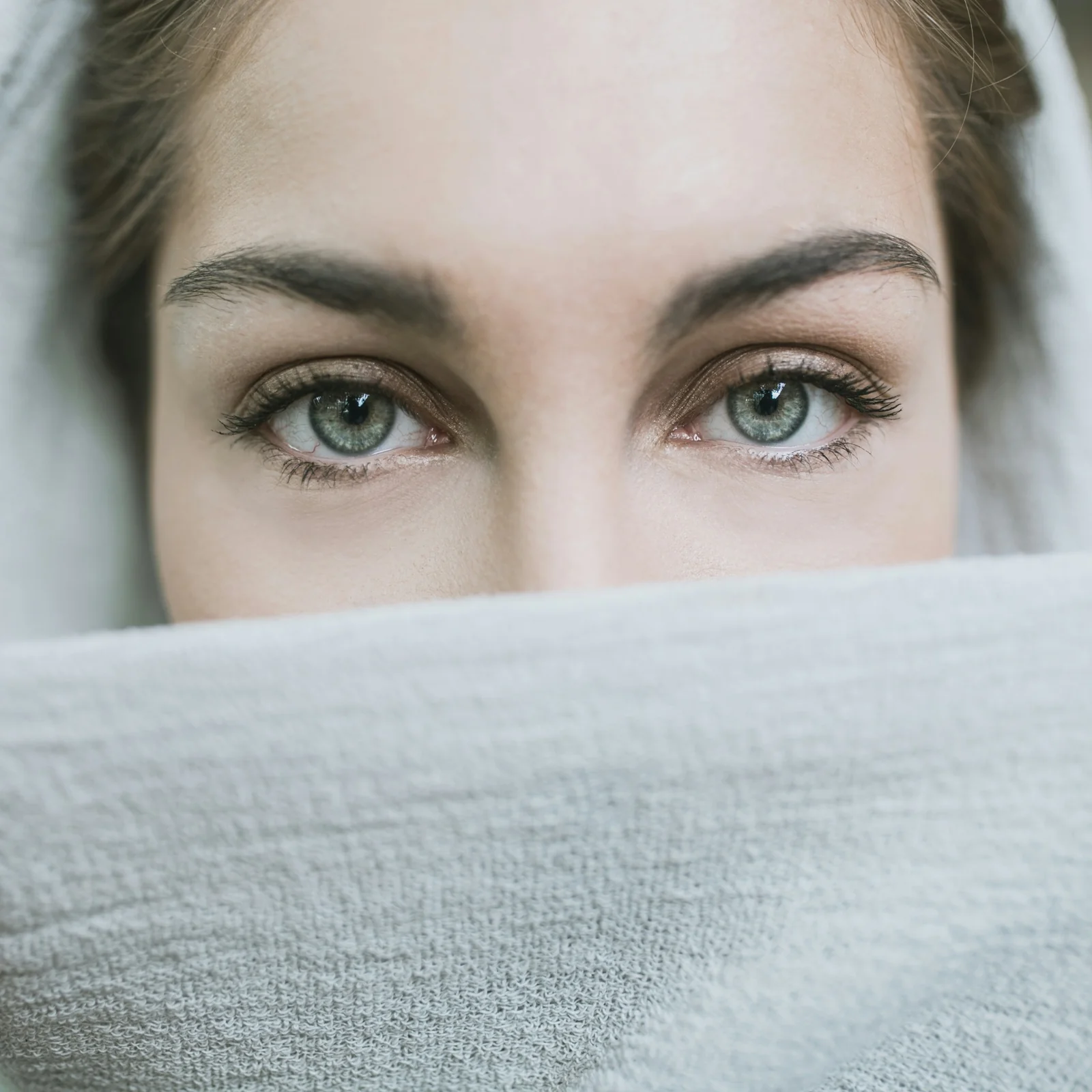 Editorial portrait of eyes and brows above a soft grey knit