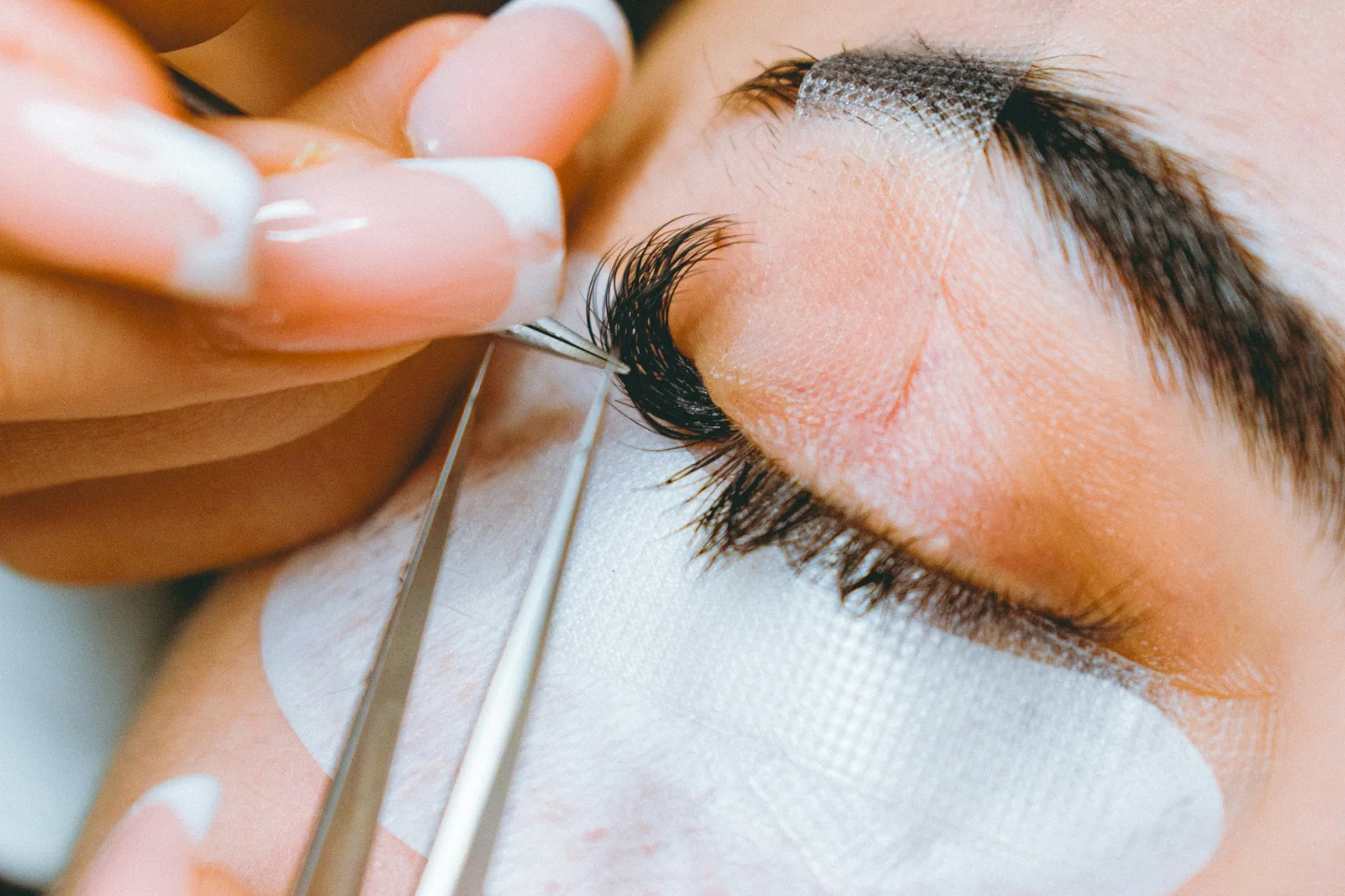 Editorial detail of a lash artist applying extensions with tweezers